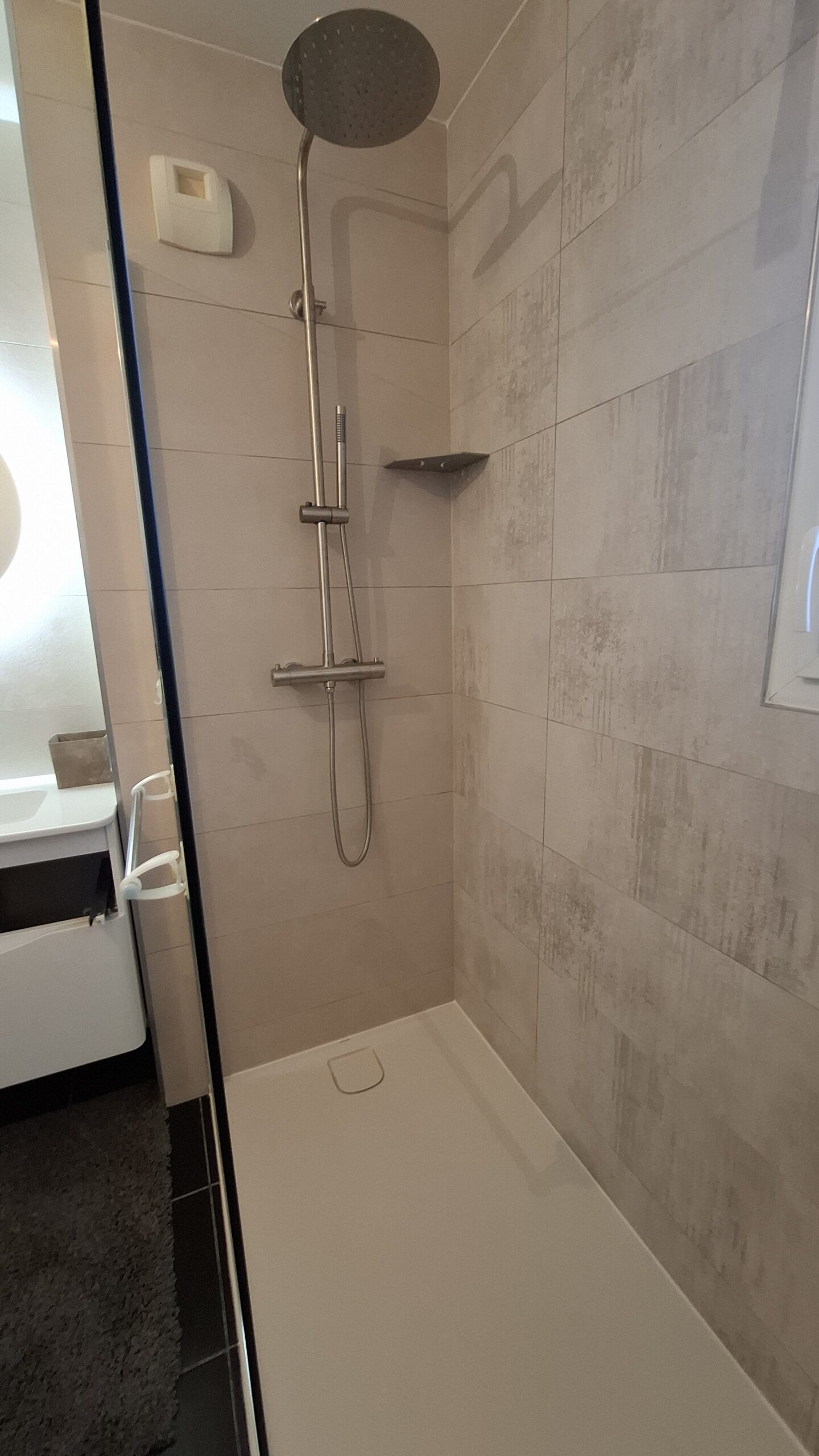 Douche avec receveur extra-plat, sol et murs carrelés, paroi en verre et finition moderne.